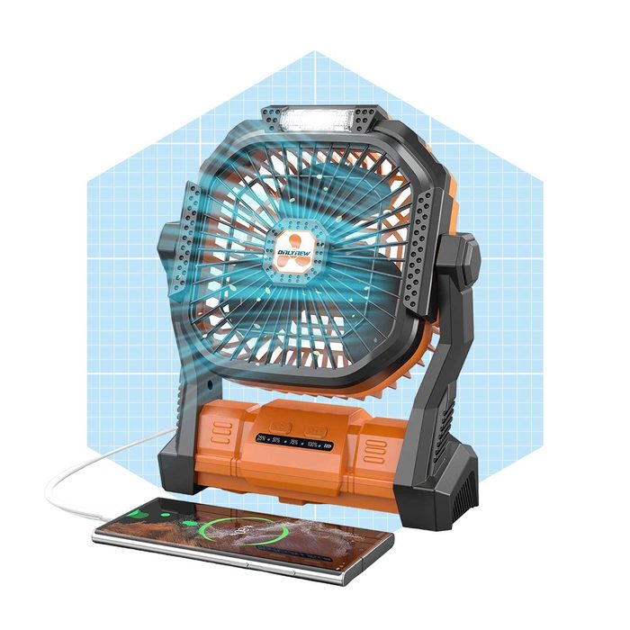 A portable fan emits airflow while charging a smartphone beside it; the fan is orange and black, set against a light blue grid background.