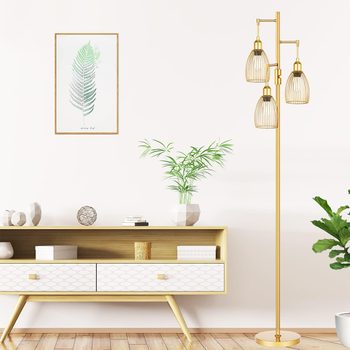 A golden floor lamp with three light fixtures stands beside a wooden console, adorned with decor and a leafy plant against a neutral wall.