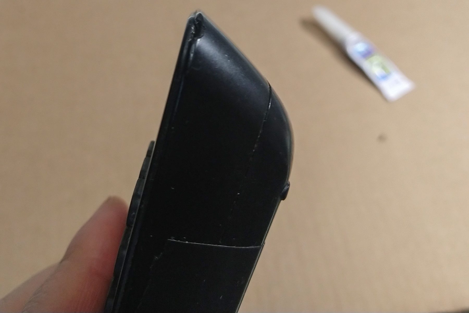 A black object with a rounded corner rests in a person's hand, showcasing a minor crack, against a beige background with a tube nearby.