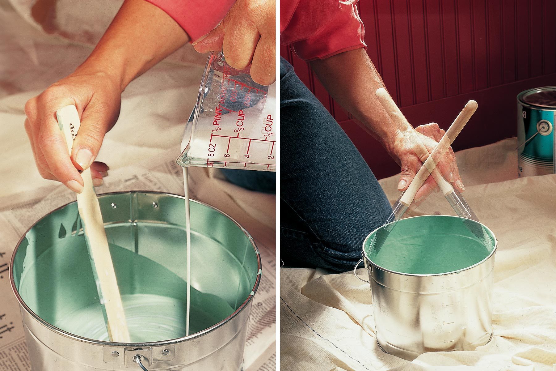A hand pours liquid from a measuring cup into a metal paint bucket, while another hand stirs with two paintbrushes on a drop cloth.